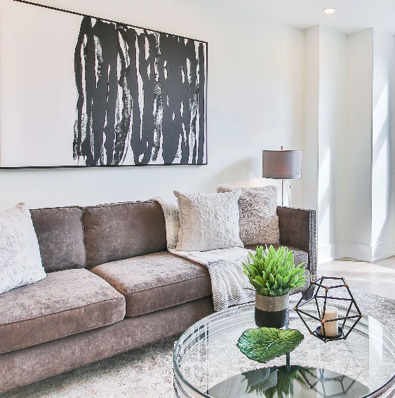 Fotografía de salón con tonalidades claras con un sofá, mesas y cojines. Gran cuadro colgado detrás